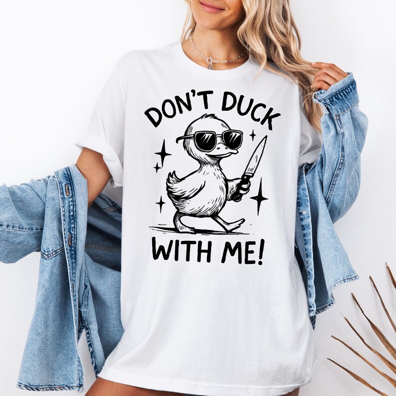 May include: White t-shirt with a black graphic of a duck wearing sunglasses and holding a knife. The text "DON'T DUCK WITH ME!" is above and below the duck illustration.