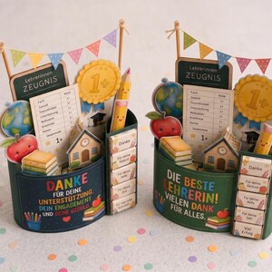 May include: Two decorative desk organisers featuring school-themed cutouts including a globe, apple, pencil, and a report card labelled Lehrerinnen ZEUGNIS. The containers are adorned with colourful bunting and German text expressing gratitude.