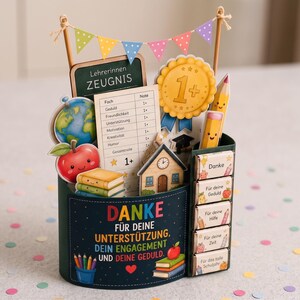 May include: A dark green desk organiser featuring school-themed decorations including a globe, an apple, a report card, a gold medal, and pencils. The front displays the text "DANKE F&Uuml;R DEINE UNTERST&Uuml;TZUNG, DEIN ENGAGEMENT UND DEINE GEDULD" with colourful bunting.
