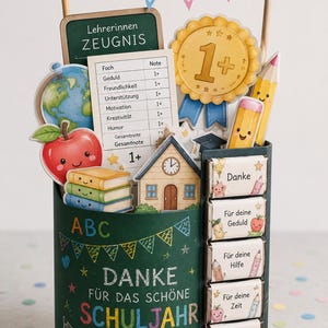 May include: A dark green cylindrical container decorated with school-themed chalk drawings and the text Danke f&uuml;r das sch&ouml;ne Schuljahr. It holds cutouts of a report card, a gold medal, a globe, an apple, books, and a schoolhouse with bunting.