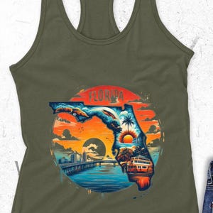 May include: Olive green racerback tank top featuring a colorful graphic of Florida's outline filled with a sunset scene, palm trees, and a bridge. The word "FLORIDA" is arched across the top of the design.