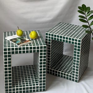 Op de afbeelding: Twee kubusvormige bijzettafels met een donkergroen en wit tegelpatroon. Op één tafel liggen een tijdschrift en twee peren. De tafels zijn aan twee zijden open. De achtergrond is een witte doek.