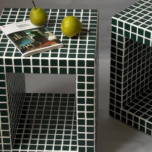 Puede incluir: Dos mesas auxiliares cuadradas con un patrón de baldosas verde oscuro y blanco. Una mesa tiene una revista y dos peras verdes encima. La otra mesa es parcialmente visible. Las mesas tienen un diseño abierto con una abertura cuadrada.