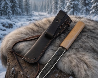 May include: A fixed-blade knife with a light-colored wooden handle and a dark, textured metal blade. The knife is accompanied by a dark brown leather sheath featuring visible stitching, a belt loop, and a thin leather cord attachment.