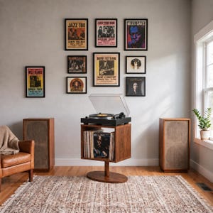 May include: A black turntable with a clear dust cover sits on a wooden stand containing vinyl records. Two tall wooden speakers flank the stand. Eight framed music posters are arranged on the wall above the turntable in a gallery display.