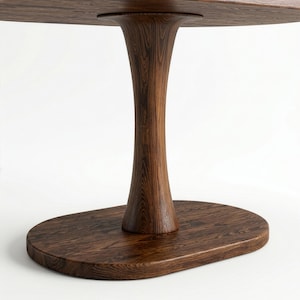 Puede incluir: Una mesa de madera de color marr&oacute;n oscuro con una base de pedestal curva y lisa que se ensancha hacia arriba y hacia abajo. La mesa presenta un patr&oacute;n de veta de madera visible en toda su superficie, apoyada sobre una base ovalada plana.