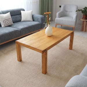 Może przedstawiać: Biały ceramiczny kubek z czarnym uchwytem i napisem "But First, Coffee" czarną, odręczną czcionką. Kubek stoi na białej powierzchni.