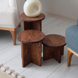 May include: Set of three wooden side tables with a rich, dark brown finish. Each table has a round top and a sturdy, geometric base. The tables vary in size, with the largest measuring approximately 18 inches in height.