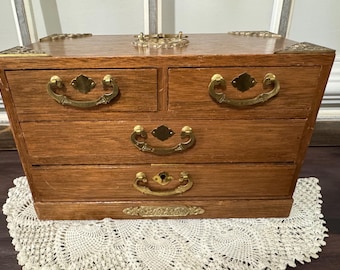 May include: A wooden jewelry box with four drawers and brass hardware. The box has a dark wood finish and is decorated with brass accents.