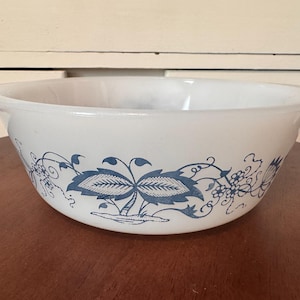 May include: White mixing bowl with a blue floral design. The bowl has a rounded shape with a wide rim and handles. The blue design features stylized leaves and flowers, adding a decorative touch to the kitchenware.