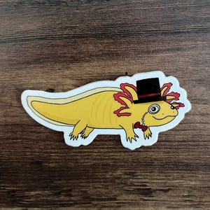 May include: A yellow axolotl wearing a black top hat with a red band, a monocle, and a red bow tie. The axolotl has red feathery gills.
