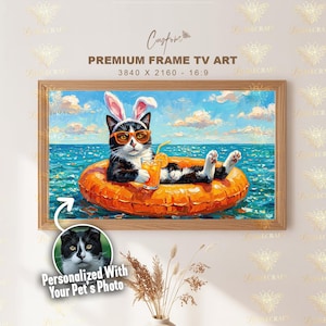 Puede incluir: Una obra de arte enmarcada representa un gato blanco y negro con gafas de sol y orejas de conejo, flotando en un flotador naranja en el océano. El gato sostiene una bebida con una pajita. La obra de arte se titula "Premium Frame TV Art."