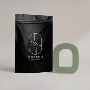 May include: A black pouch with a zipper closure and the word "PODERN" in white, along with a geometric design. Next to it is a sage green, arched-shaped object. The text on the pouch reads "PODS MADE MODERN."