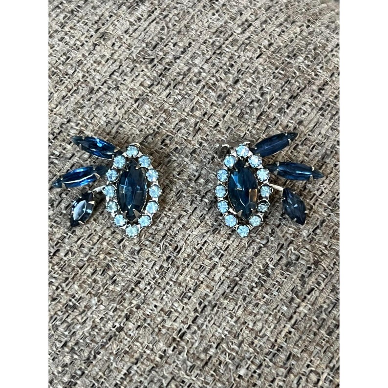 May include: A pair of vintage clip-on earrings with a blue oval rhinestone surrounded by smaller clear rhinestones and a cluster of blue rhinestones on each side.