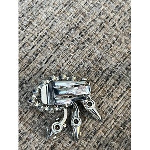 May include: A silver tone clip-on earring with a cluster of clear rhinestones and a 'Coro Jewels' marking on the back.