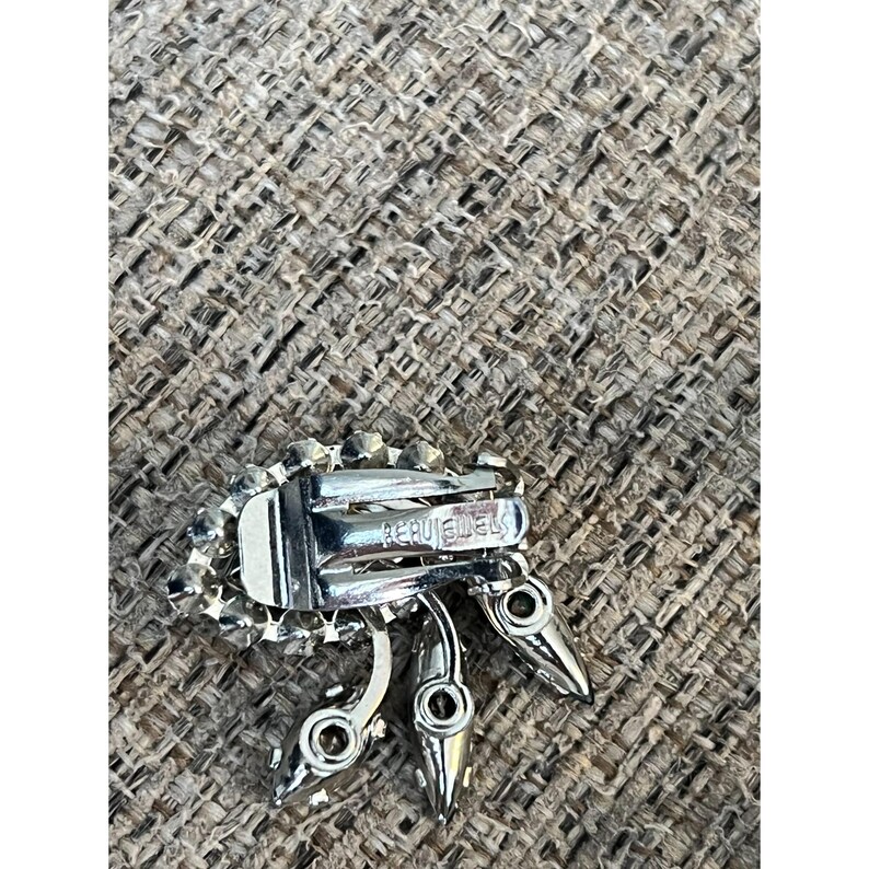 May include: A silver tone clip-on earring with a cluster of clear rhinestones and a 'Coro Jewels' marking on the back.