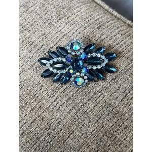 May include: A vintage brooch with a cluster of dark blue and light blue rhinestones in a floral design.