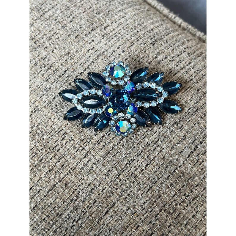 May include: A vintage brooch with a cluster of dark blue and light blue rhinestones in a floral design.