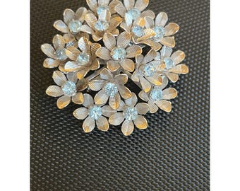 May include: A silver brooch with a cluster of small, white flowers with blue rhinestone centers.