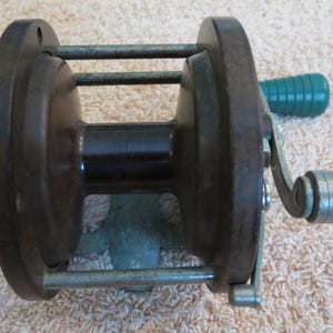 May include: A vintage wooden fishing reel with a green plastic handle and a metal crank. The reel has a dark brown finish and a metal frame.