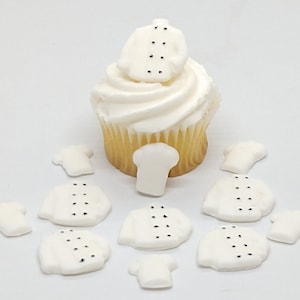 Op de afbeelding: Witte fondant cupcake-toppers in de vorm van koksjassen met zwarte stippen. Er zijn in totaal 10 toppers, waarvan er één op een geglazuurde cupcake zit.