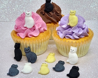 以下が含まれることがあります： 紫、ピンク、茶色のフロスティングで飾られた3つのカップケーキ。各カップケーキには、白、黒、黄色のさまざまな色の小さなフォンダン製の猫の置物が飾られています。カップケーキの周りには、さまざまな色のフォンダン製の猫の置物がいくつか散らばっています。
