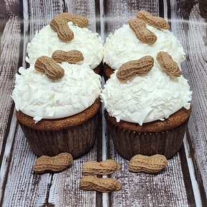 May include: Four cupcakes topped with white frosting and shredded coconut. Each cupcake is decorated with several peanut-shaped candies.