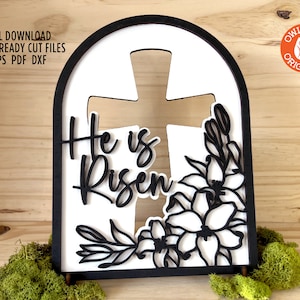 May include: Black and white laser cut wooden sign with an arched top. The sign features a cross with the words "He is Risen" and a floral design.