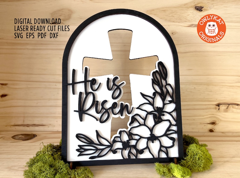 May include: Black and white laser cut wooden sign with an arched top. The sign features a cross with the words "He is Risen" and a floral design.