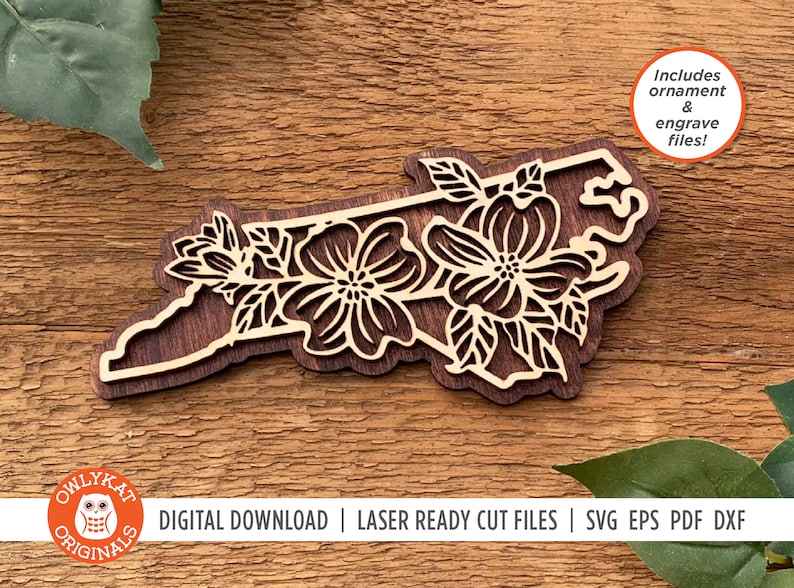 May include: A laser cut wooden ornament of the state of North Carolina with floral designs. The ornament is on a wooden surface. The text "Includes ornament & engrave files!" is in the upper right corner of the image. The text "DIGITAL DOWNLOAD | LASER READY CUT FILES | SVG EPS PDF DXF" is at the bottom of the image.