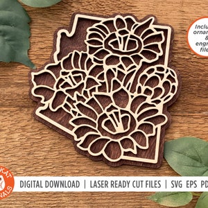 May include: A laser cut wooden cutout of the state of Arizona with a floral design inside. The design features three large flowers with intricate details. The cutout is brown and has a light wood background. The text "Includes ornament & engrave files!" is in a white circle on the right side of the image. The text "OWLYKAT ORIGINALS DIGITAL DOWNLOAD | LASER READY CUT FILES | SVG EPS PDF DXF" is at the bottom of the image.