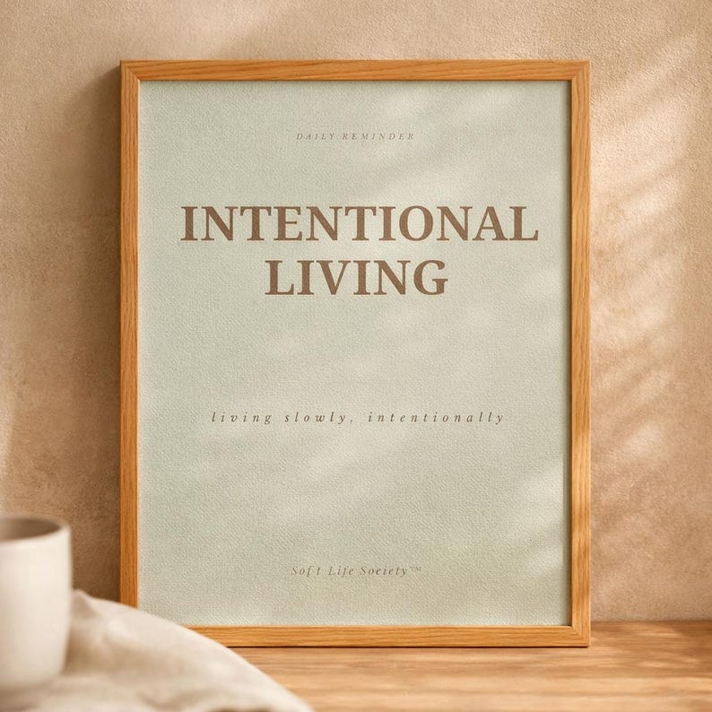 Close-up detail of minimalist affirmation poster reading “INTENTIONAL LIVING” showing elegant serif typography, subtle paper texture, and natural wood frame in warm editorial sunlight. Soft luxury printable wall art styling
