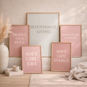 Layered printable affirmation posters including “INTENTIOAL LIVING” arranged on light wood floor with neutral decor elements such as ceramic mug, pampas grass, books, and linen fabric. Feminine quiet luxury printable wall art bundle styling.
