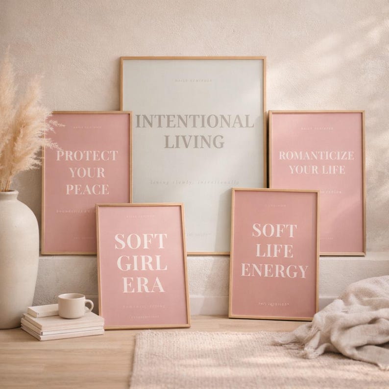 Layered printable affirmation posters including “INTENTIOAL LIVING” arranged on light wood floor with neutral decor elements such as ceramic mug, pampas grass, books, and linen fabric. Feminine quiet luxury printable wall art bundle styling.