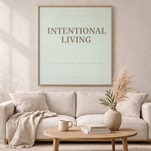 Framed printable affirmation poster reading “INTENTIONAL LVING” styled in a modern minimalist home setting with neutral decor, soft linen textures, ceramic mug, pampas grass, and warm morning light creating a peaceful soft life atmosphere.