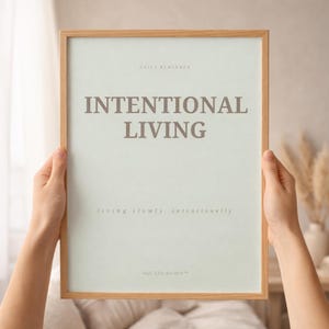 Close-up detail of minimalist affirmation poster reading “INTENTIONAL LIVING” showing elegant serif typography, subtle paper texture, and natural wood frame in warm editorial sunlight. Soft luxury printable wall art styling
