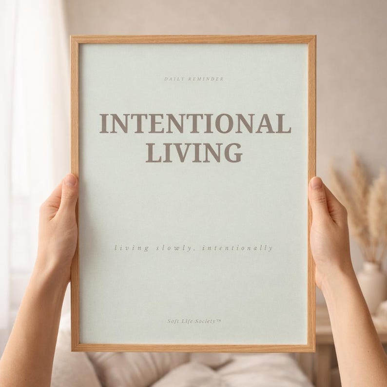 Close-up detail of minimalist affirmation poster reading “INTENTIONAL LIVING” showing elegant serif typography, subtle paper texture, and natural wood frame in warm editorial sunlight. Soft luxury printable wall art styling