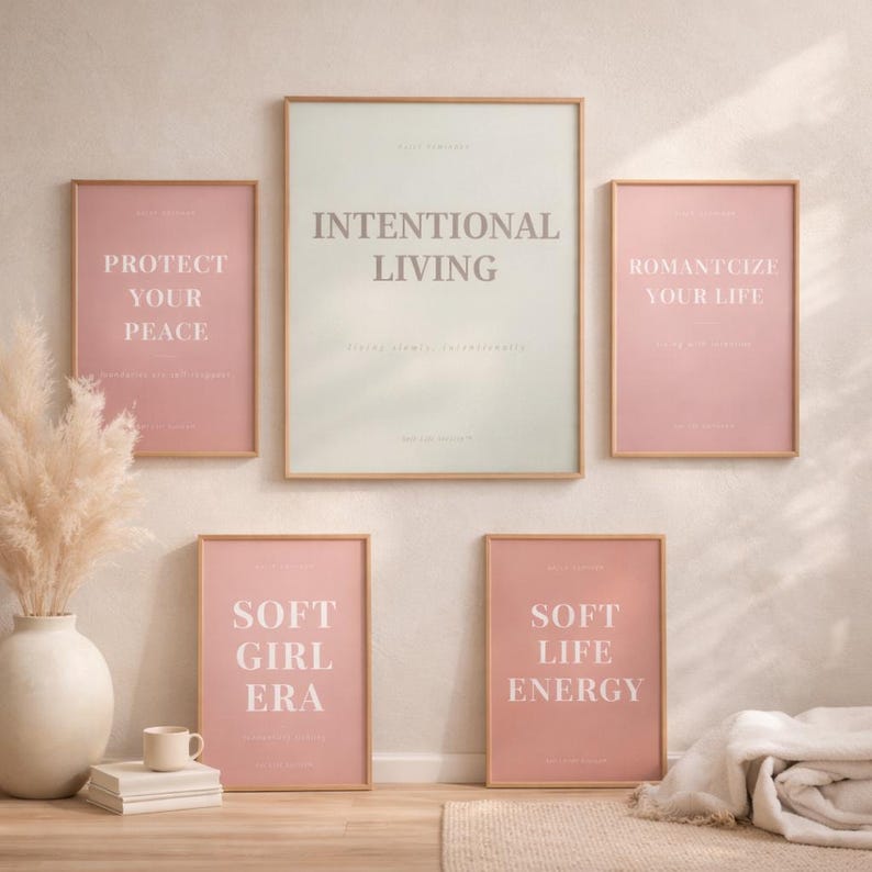 Set of minimalist affirmation posters including “INTENTIONAL LIVING” arranged in a Scandinavian gallery wall display with light wood frames, textured neutral wall, and soft editorial sunlight. Modern soft living home decor styling.
