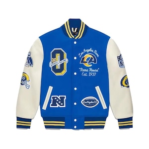 Puede incluir: Una chaqueta de béisbol azul y blanca con varios parches, incluyendo una gran "O" con "OCTOBER'S VERY OWN" escrito en su interior, un logotipo de los Los Angeles Rams con "Rams House" y "Est. 1937" escrito debajo, y una "N" con estrellas.