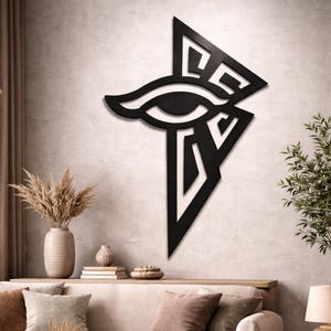 May include: A black wooden wall art piece featuring the Eye of Horus symbol. The artwork is mounted on a textured, light-colored wall. The eye is a stylized design with a triangular shape below it.