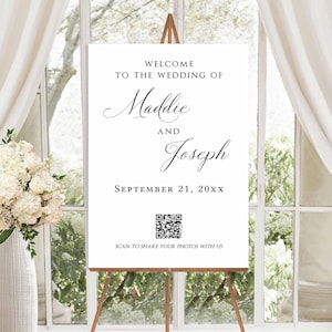 May include: A white wedding welcome sign on a wooden easel. The sign reads "Welcome to the Wedding of Maddie and Joseph, September 21, 20XX." A QR code is at the bottom with the text "Scan to share your photos with us."