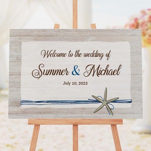 May include: A wooden wedding sign with a rustic background and blue and white ribbon. The sign reads "Welcome to the wedding of Summer & Michael July 10, 2023".