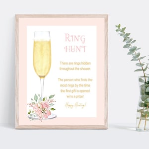 May include: A pink and gold printable sign with a champagne glass and floral design. The text reads "RING HUNT" and includes instructions for a ring hunt game.