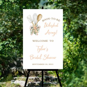 Puede incluir: Un letrero blanco sobre un caballete negro con texto e ilustraciones para una despedida de soltera. El letrero dice "SOON-TO-BE Whisked Away!" y "WELCOME TO Tylar's Bridal Shower" con la fecha "SEPTEMBER 24, 20XX". La parte superior presenta un batidor, una espátula y una cuchara.
