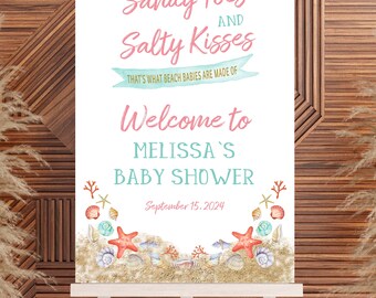 May include: A white sign with a pink and blue beach-themed baby shower announcement. The sign reads "Sandy Toes and Salty Kisses That's what beach babies are made of. Welcome to Melissa's Baby Shower September 15, 2024". The sign is decorated with seashells, starfish, and coral.