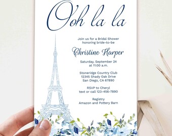 May include: Bridal shower invitation with the text "Ooh la la" in navy blue script. Features a light blue Eiffel Tower illustration and floral accents. Includes event details: date, time, location, and RSVP information.