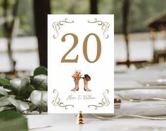 May include: White table number card with the number 20 in a gold color. The card features a watercolor illustration of cowboy boots and a hat, with the names Alani & Nathan below. Decorative gold flourishes frame the top and bottom.