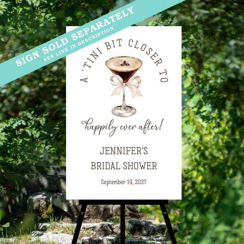 Puede incluir: Cartel blanco sobre un caballete negro con el texto "A 'Tini Bit Closer To" y "Happily ever after!" con una ilustraci&oacute;n de acuarela de un martini. El cartel es para la despedida de soltera de Jennifer, 19 de septiembre de 2037.