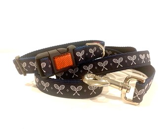 May include: Navy blue dog collar and leash set with a white tennis racket pattern. The collar has a black buckle with an orange reflector. The leash has a silver metal clasp.
