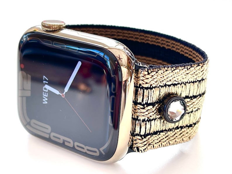 May include: A gold Apple Watch with a black and gold patterned band. The watch face displays the date and time, with the day of the week shown as "WED 17".